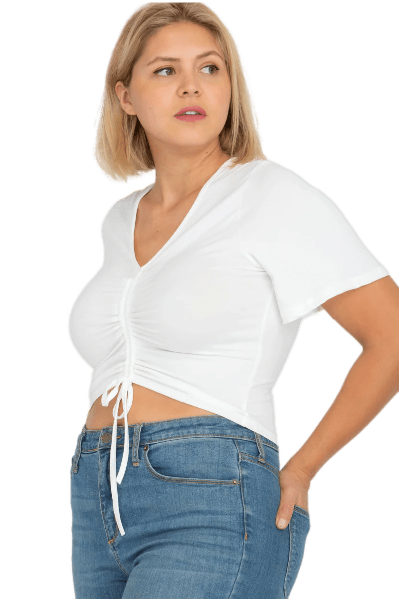 Plus size model wearing a white strap ruched front short sleeve crop top with flared sleeves and jeans.