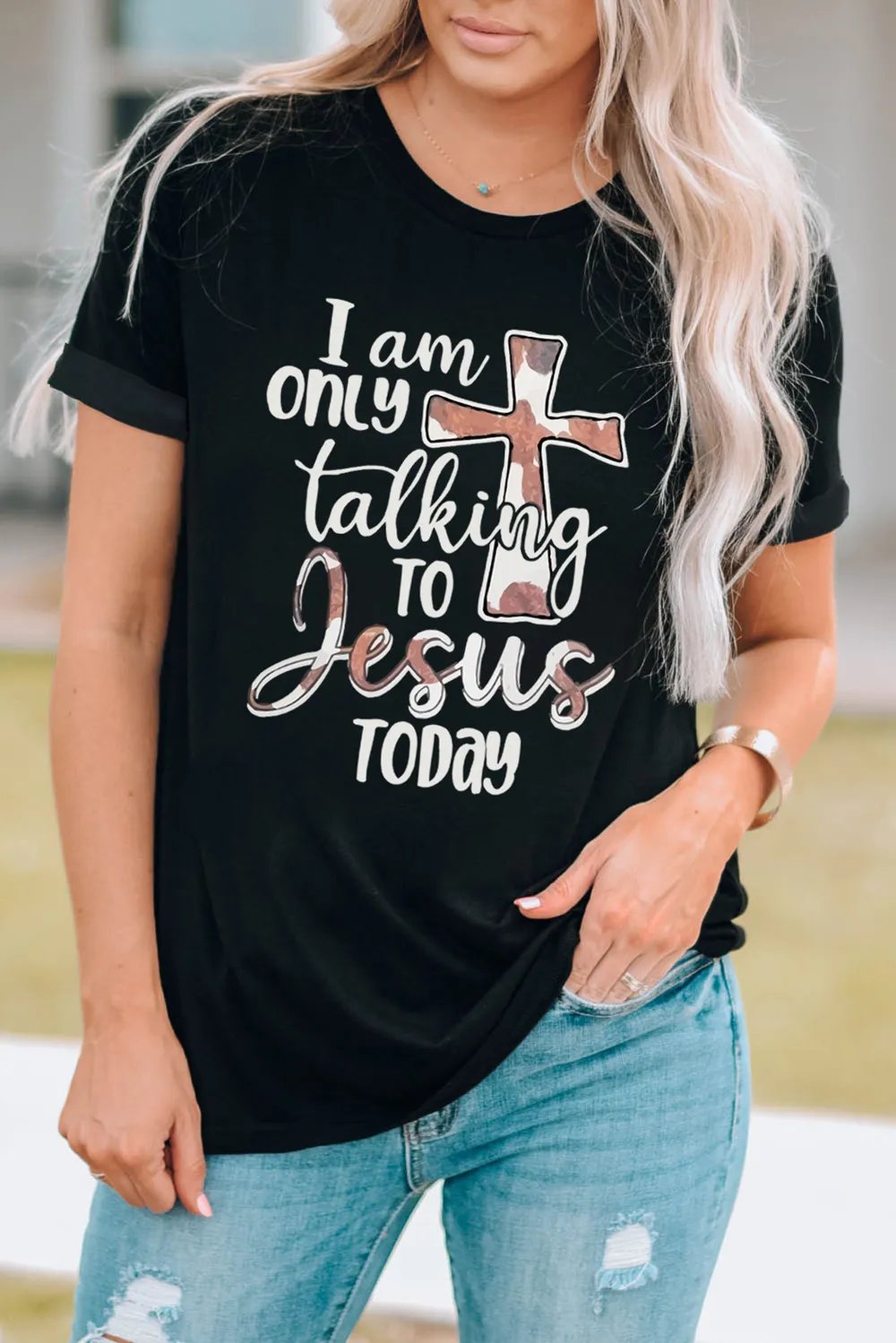 Woman wearing black graphic tee with "I am only talking to Jesus today" design, paired with ripped jeans and casual style.