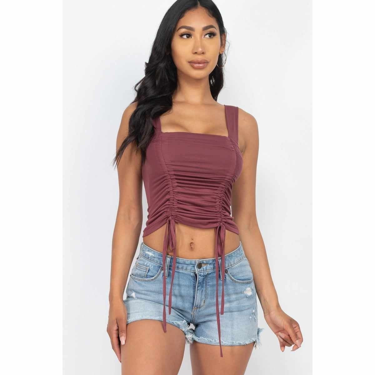 Woman in trendy maroon ruched crop top and denim shorts, showcasing stylish casual wear for women.