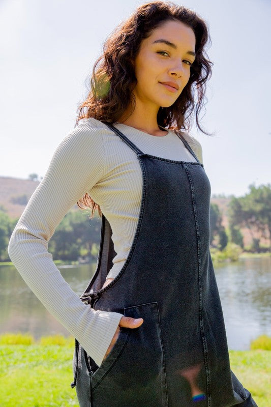 Woman wearing black drawstring waist spaghetti strap overalls with pockets outdoors near a lake.