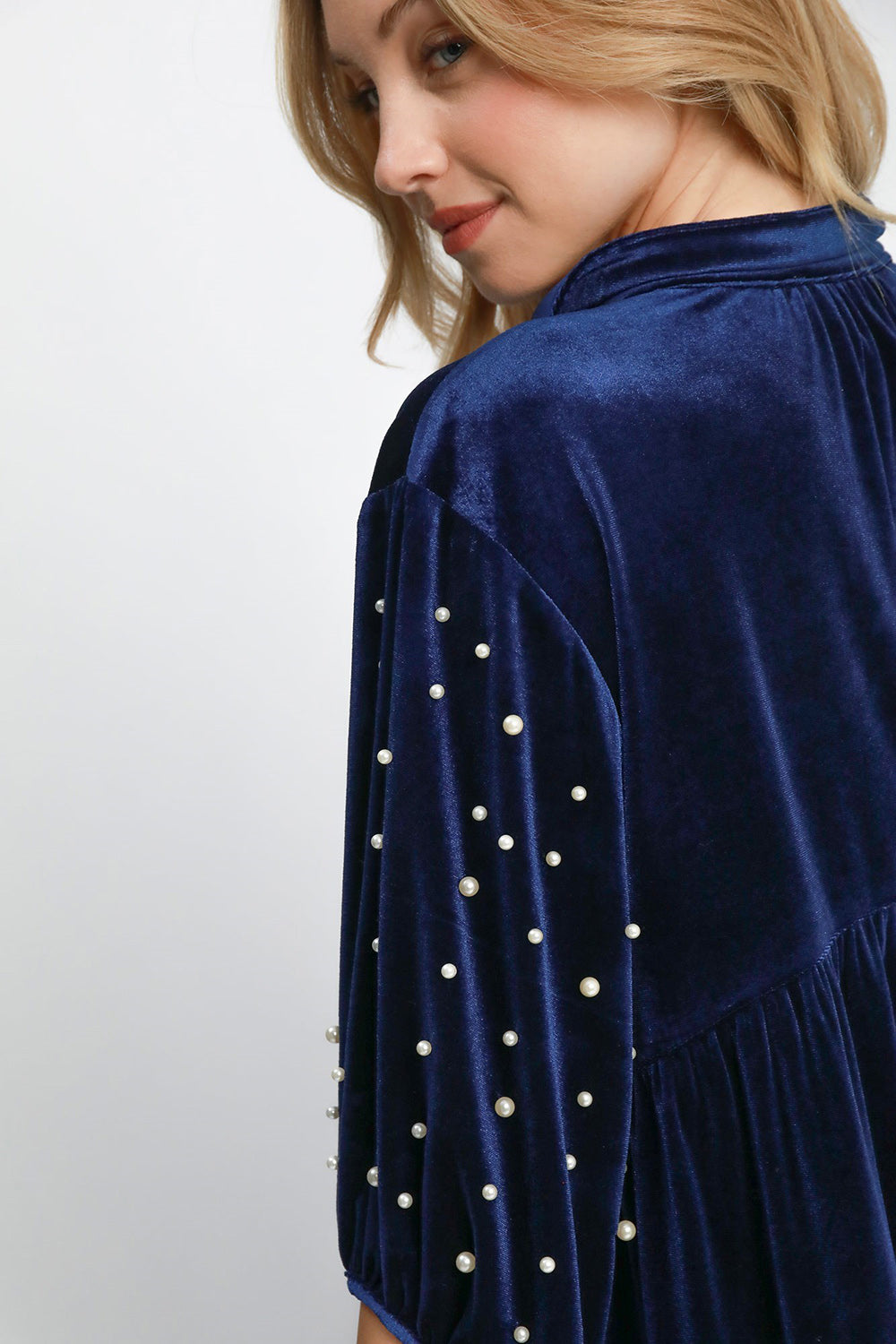 Woman wearing navy velvet blouse with pearl details and collared neck, featuring ruched, buttoned design, slightly stretchy material.