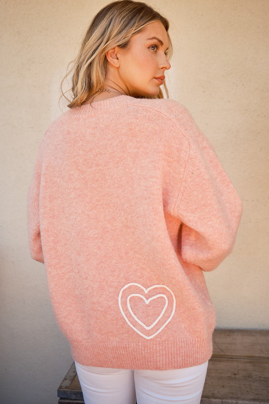 Woman wearing a pink WIFEY sweater with heart design, round neck, made of polyester, wool, and spandex.