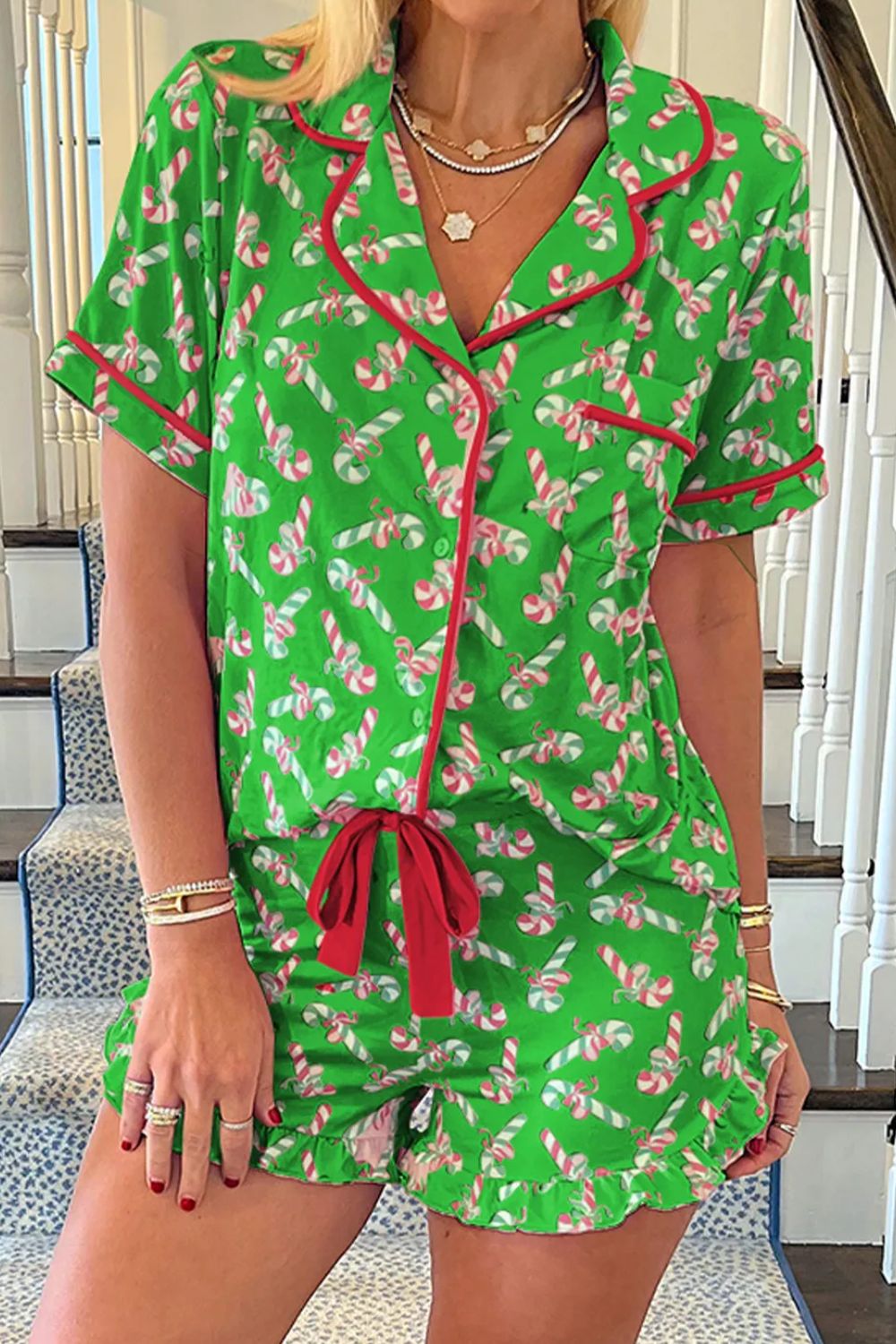 Woman wearing green candy cane collared neck top and shorts pajama set with red trim, standing on stairs.