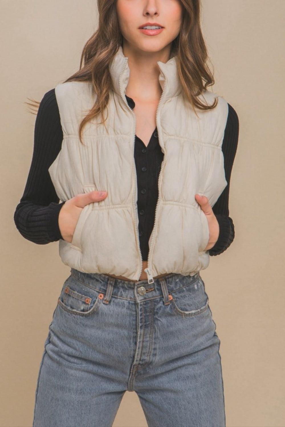 Woman wearing cream zip-up turtleneck cropped vest coat with a black top and jeans.