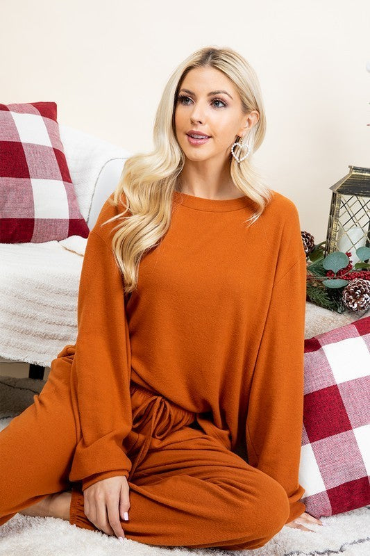 Rust-colored fuzzy lounge set with round neck top and pants, featuring 68% polyester blend, worn by model in cozy setting.