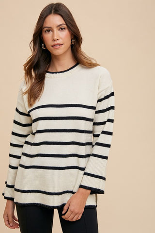 Woman wearing an ivory side-slit striped round-neck sweater with black stripes, featuring a basic style and ribbed design