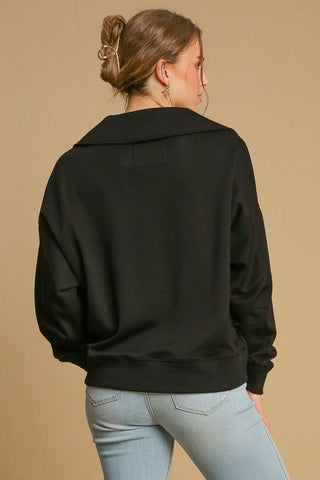 Woman wearing black Johnny collar dropped shoulder sweatshirt, back view, paired with light jeans.