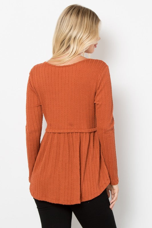 Woman wearing rust full-size knit top with round neck, long sleeves, and peplum back detail.