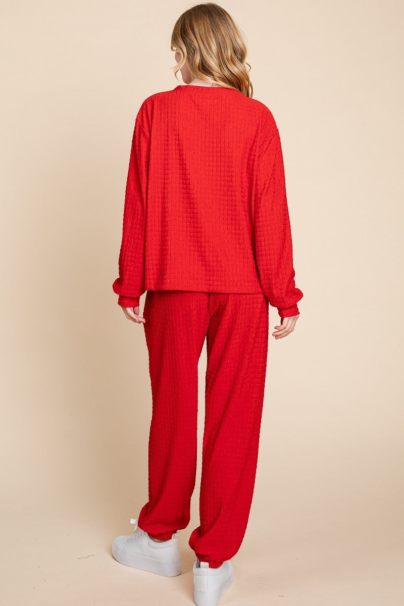 Woman modeling red full-size crinkle check lounge set with round neck top and pants, slightly stretchy fabric, casual style.