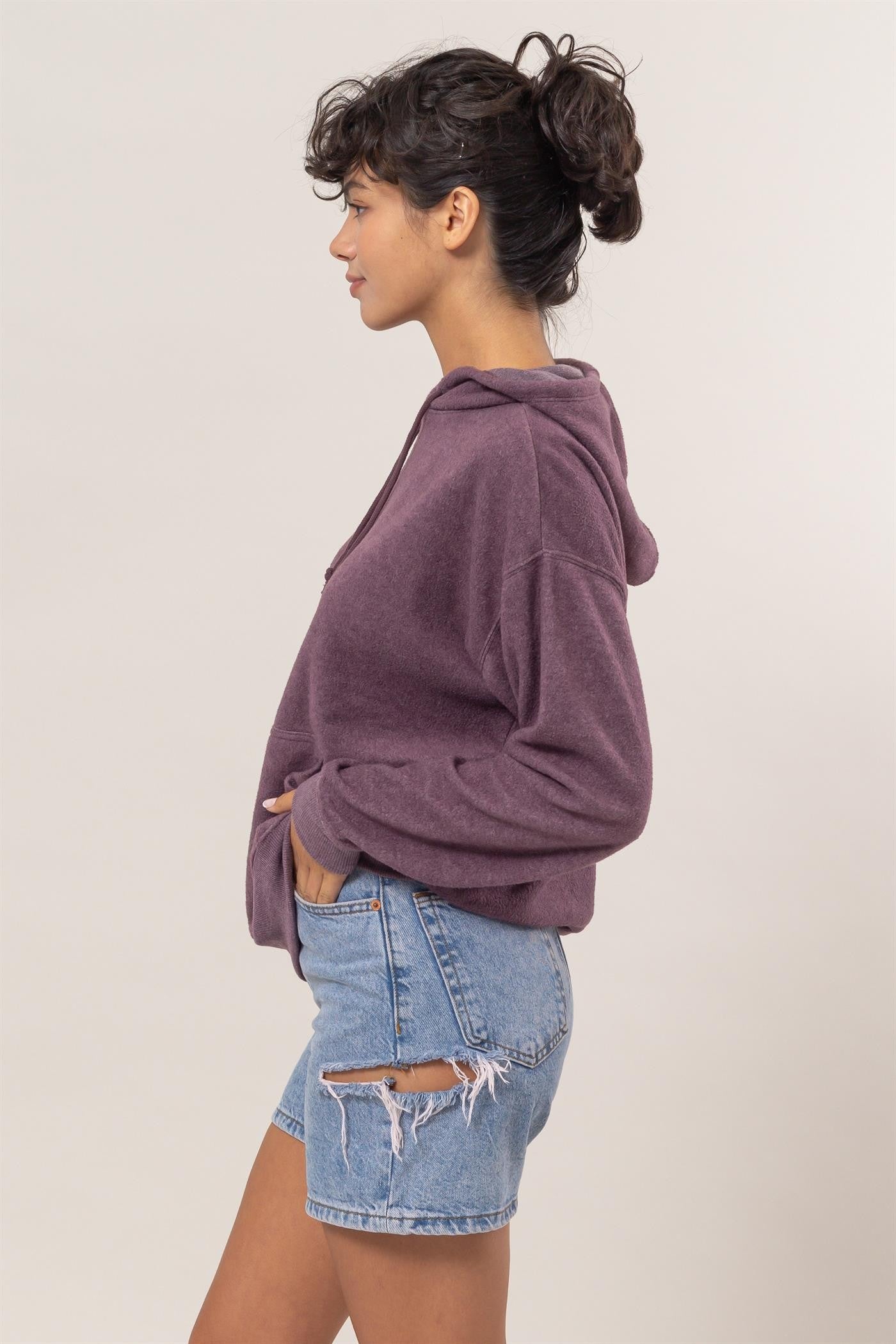 Woman wearing dark plum brushed long sleeve hoodie with kangaroo pocket and denim shorts.