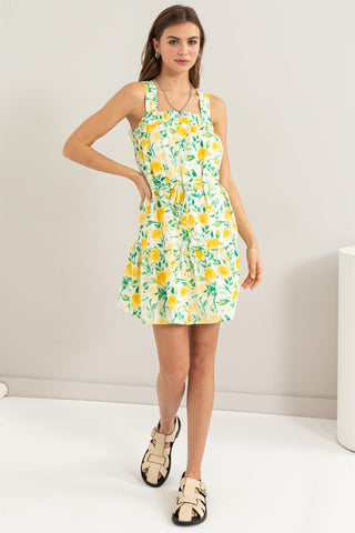 Woman wearing yellow floral tie shoulder mini dress with ruched detailing, 100% cotton, no stretch, casual summer style.