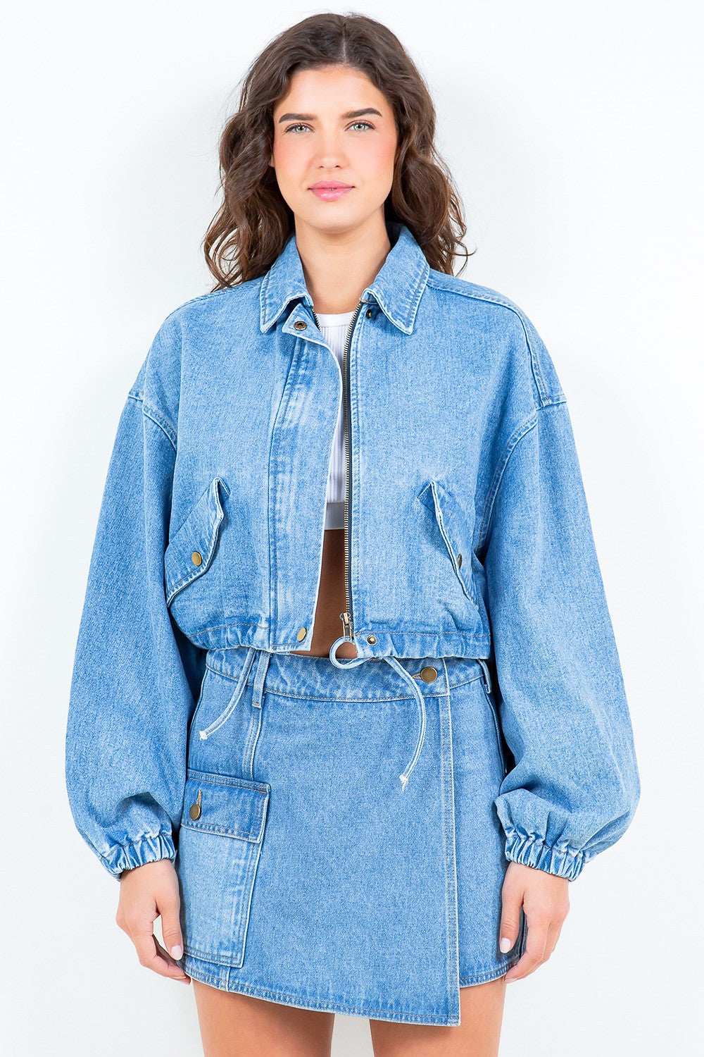 Woman wearing American Bazi drawstring waist crop denim jacket with zip closure and elastic cuffs, paired with a matching denim skirt.