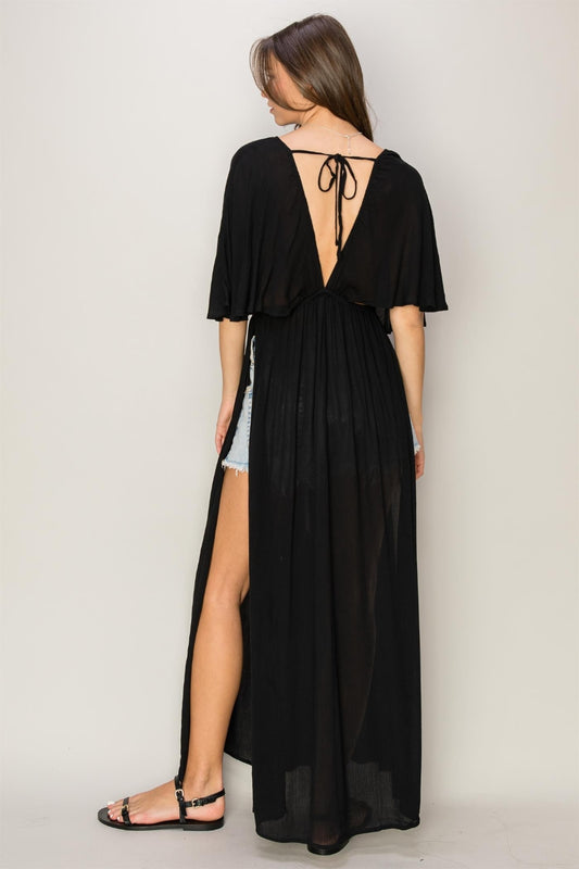 Woman in black tie back maxi dress with ruffled and slit design, showcasing backless style and opaque 100% rayon fabric.