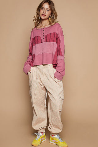 Woman wearing Cerise Half Button Color Block Drop Shoulder Knit Top with waffle-knit and eyelet design, paired with beige pants.