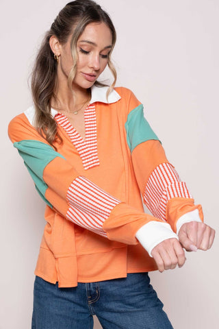 Woman wearing coral color block top with striped panel, long sleeves, and collared neckline paired with jeans.