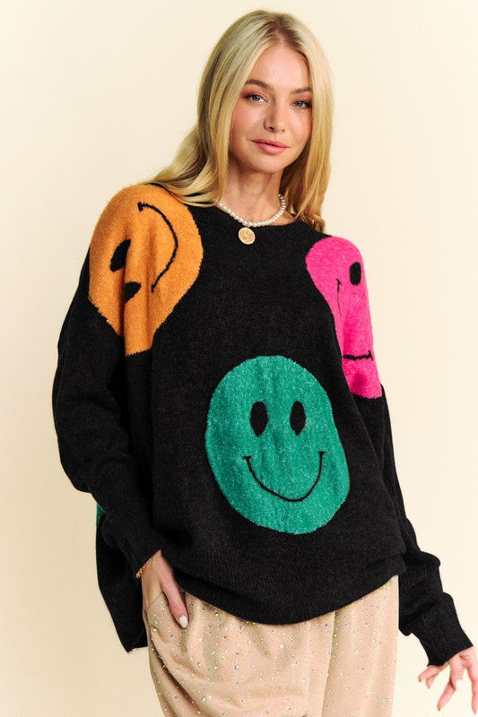 Woman wearing black oversize sweater with colorful smiley faces, round neck design, and slightly stretchy material.