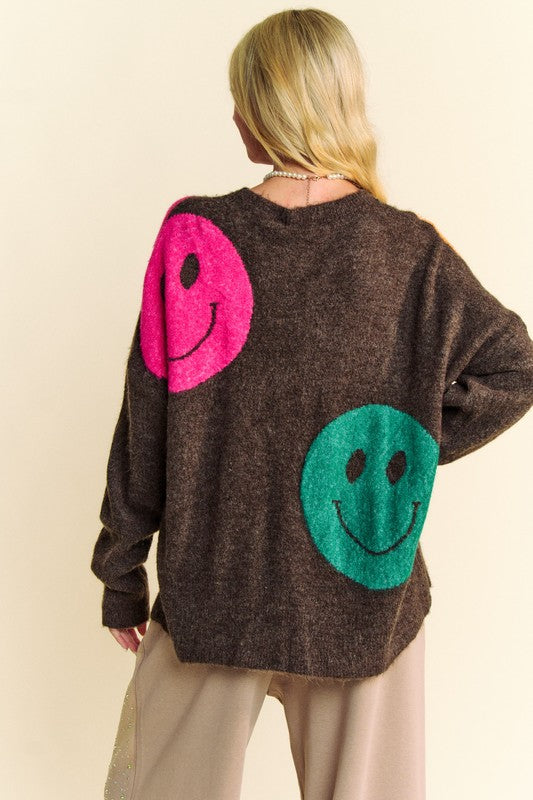 Woman wearing a contrast smile round neck oversize sweater with pink and green smiley faces, made of acrylic, polyester, and spandex.