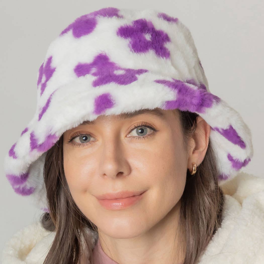 Woman wearing a floral printed faux fur bucket hat with purple designs, featuring flat top and adjustable strings, made from 100% polyester.