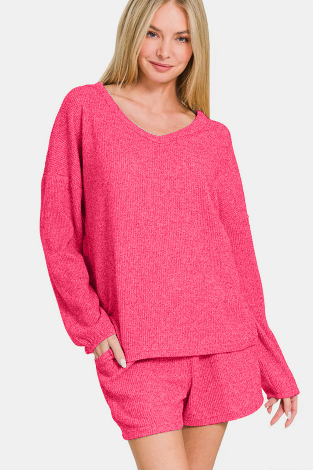 Woman wearing Zenana V-Neck Long Sleeve Ribbed Top and Shorts Set in pink, showcasing trendy and comfortable casual style.