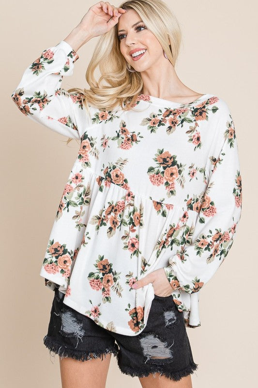 Woman wearing a floral boat neck long sleeve babydoll blouse with peplum design and distressed black shorts.