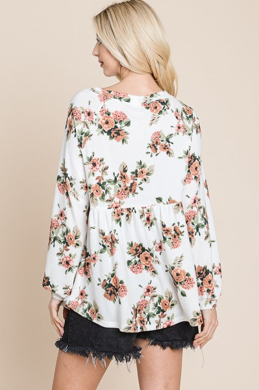 Woman wearing floral full-size babydoll blouse with boat neck and long sleeves, showcasing back view of the outfit.