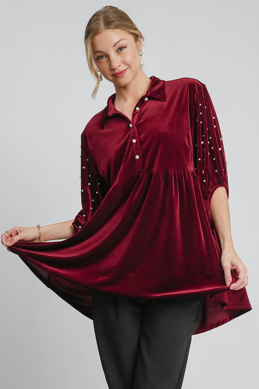 Woman wearing a pearl detail collared neck velvet babydoll blouse with tiered design and buttoned front in rich burgundy shade.