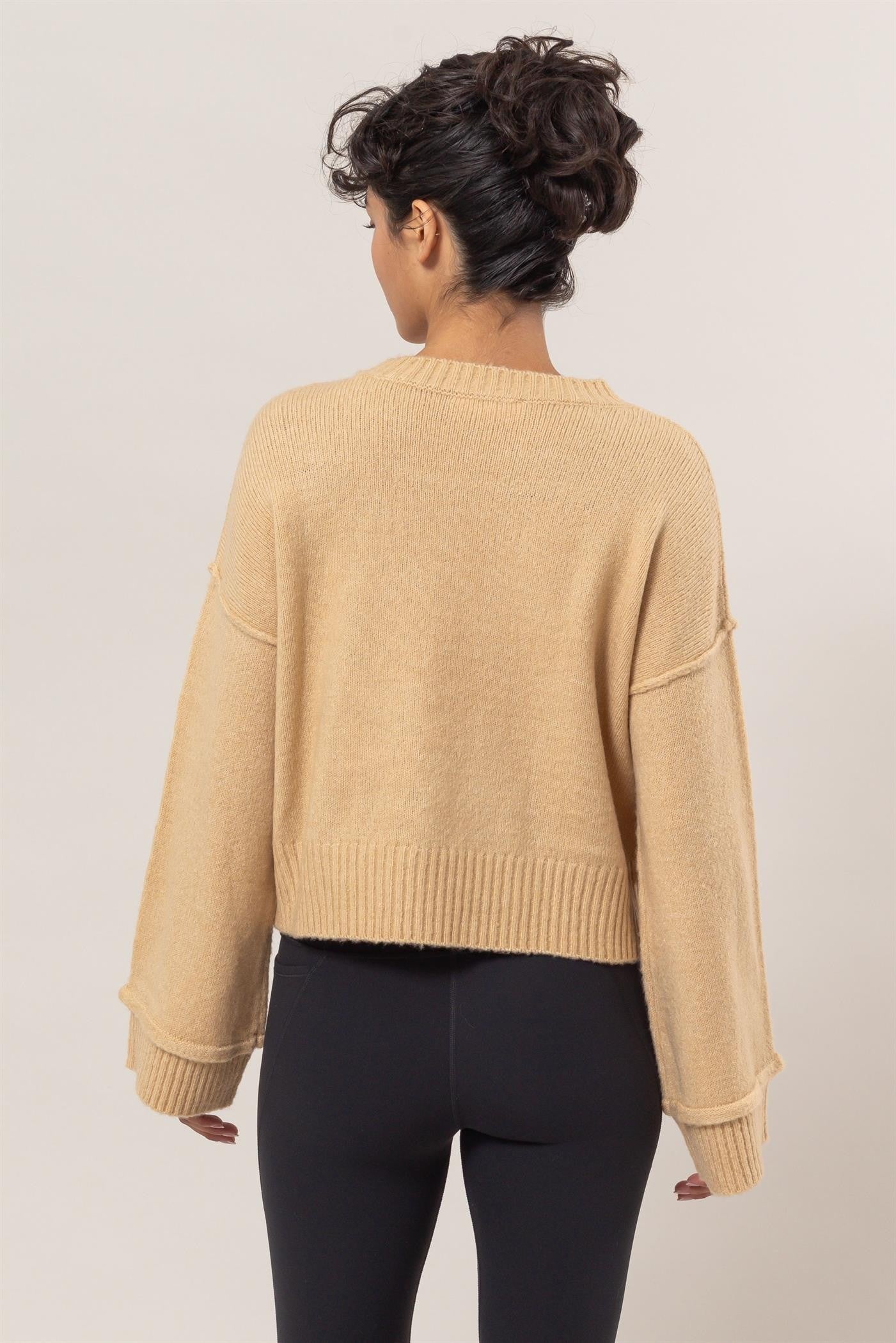 Woman wearing beige round neck dropped shoulder ribbed sweater, showcasing back view and relaxed fit.