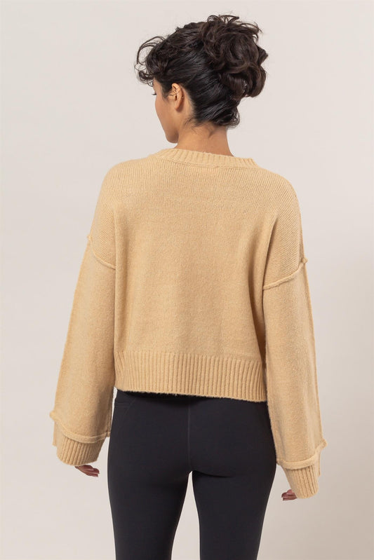 Woman wearing beige round neck dropped shoulder ribbed sweater, showcasing back view and relaxed fit.