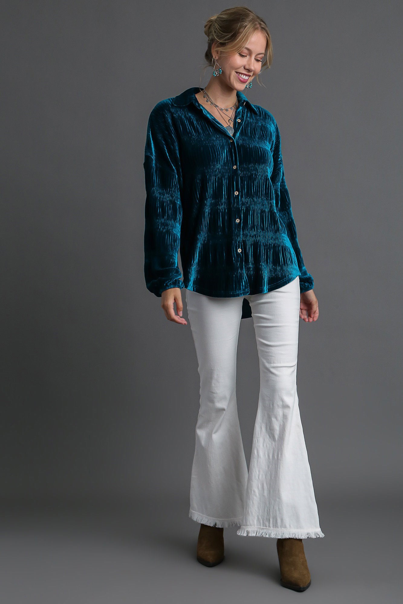 Woman wearing teal ruched tiered button-up shirt with white flared pants and brown boots.