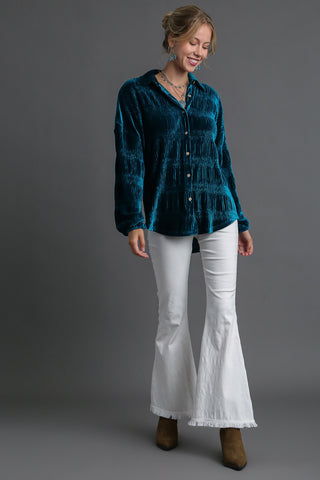 Woman wearing teal ruched tiered button-up shirt with white flared pants and brown boots.