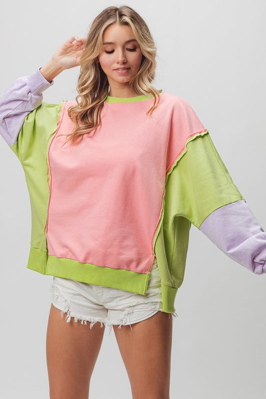 Woman wearing a Cool Washed Color Block Sweatshirt with slit and exposed seam, featuring pink, green, and purple panels.