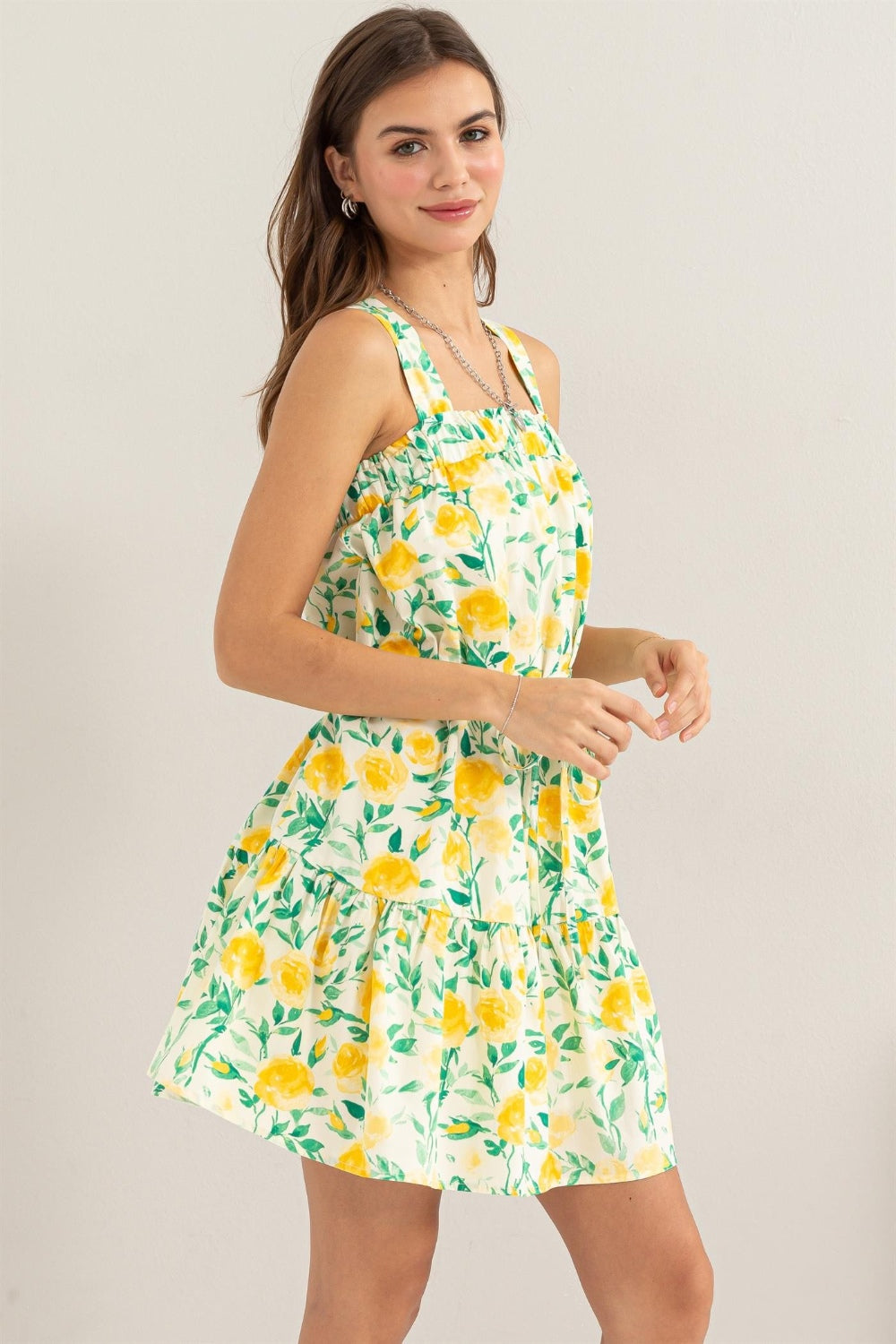 Woman wearing a yellow floral tie shoulder mini dress made of 100% cotton, featuring a ruched design and a no-stretch opaque fabric.