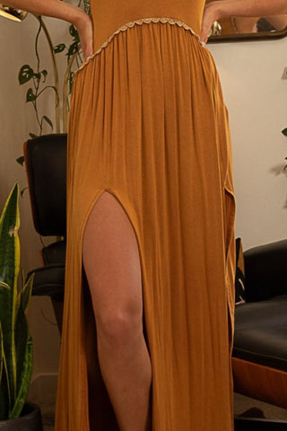 Elegant toffee sleeveless maxi dress with back zipper and front slit, made of rayon and spandex, styled in a cozy sitting room.