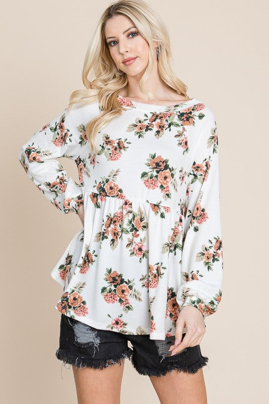 Woman wearing floral babydoll blouse with boat neck and long sleeves, paired with black shorts.