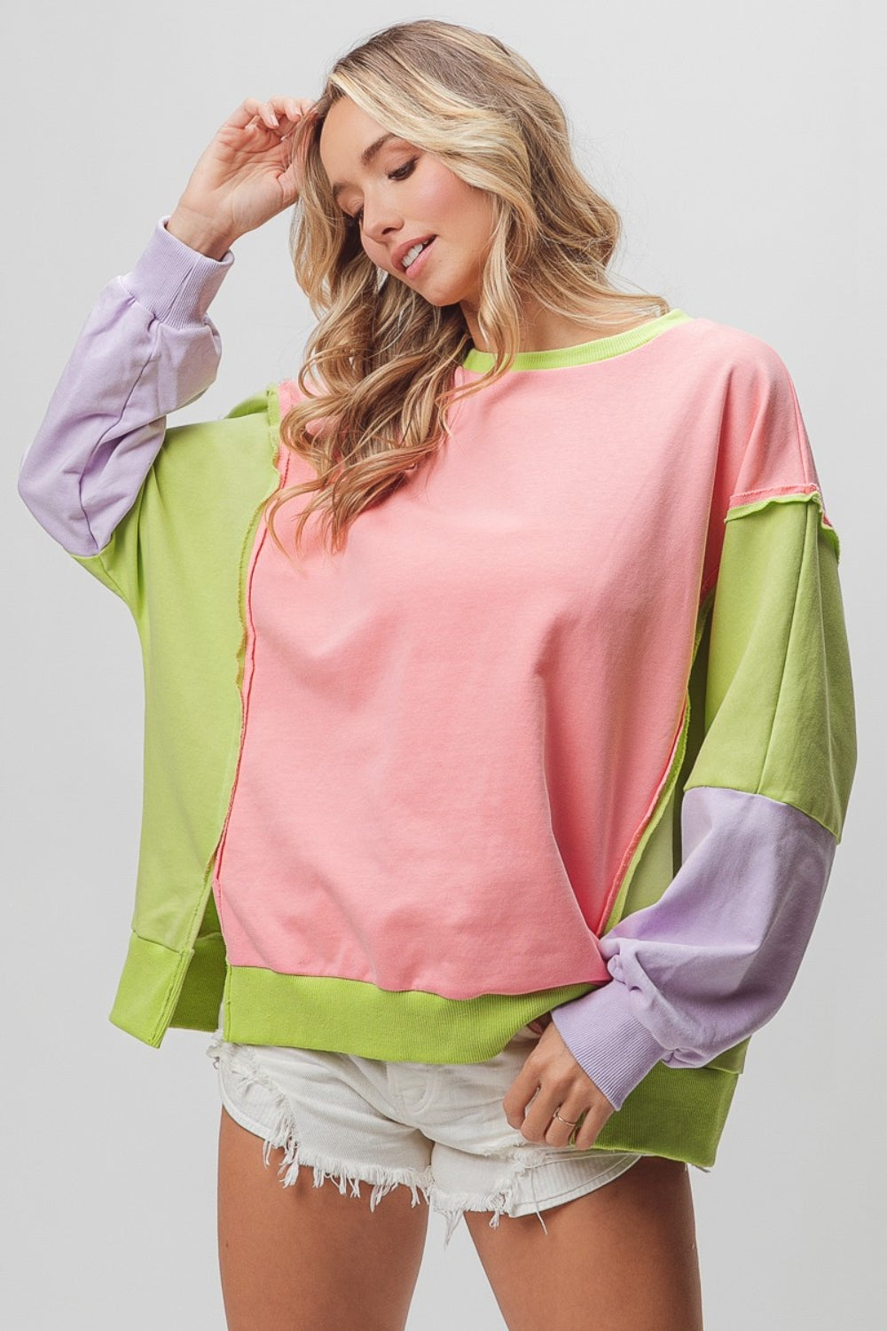 Woman wearing a cool washed color block sweatshirt in pink, green, and purple, featuring slit and exposed seam design.