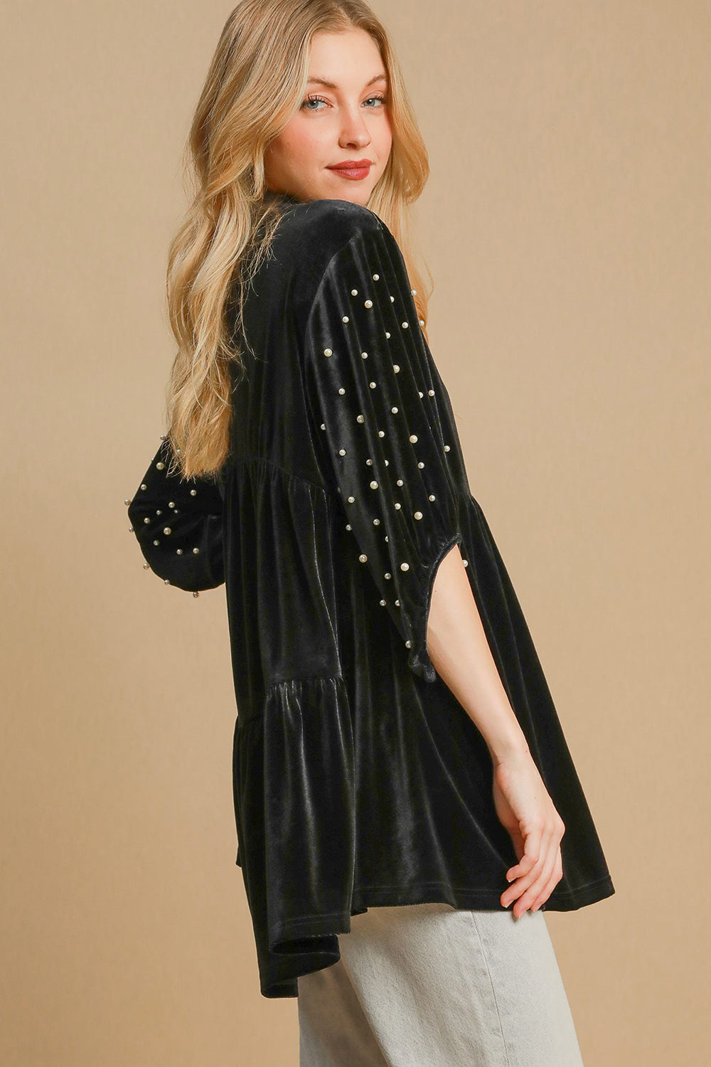 Woman wearing a black velvet babydoll blouse with pearl details and half sleeves, showcasing a tiered and ruched design.