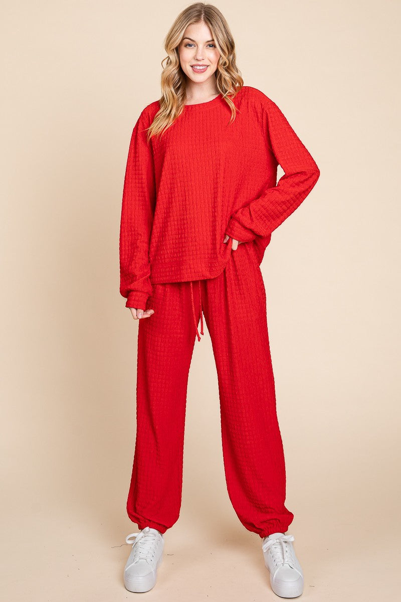 Woman wearing red crinkle check lounge set with round neck top and drawstring pants standing indoors.