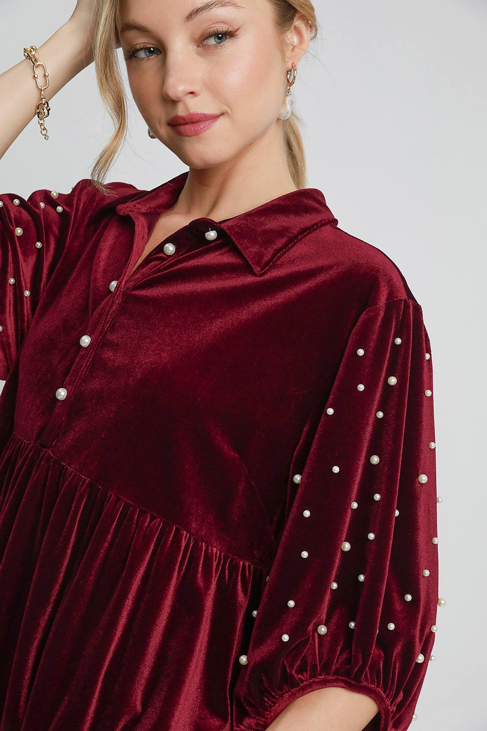 Velvet babydoll blouse with pearl details, featuring a collared neck, tiered ruched design, and buttoned high-low hem.