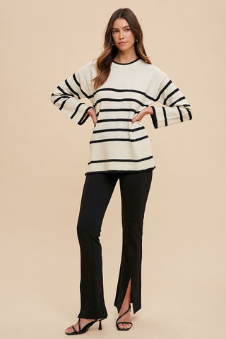 Woman wearing ivory side slit striped round neck sweater with black pants, showcasing a chic and versatile fashion look.