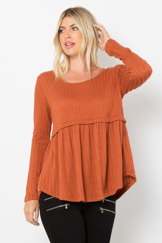 Rust knit babydoll top with round neck and long sleeves, featuring cable-knit texture and peplum style, made of polyester, rayon, spandex.