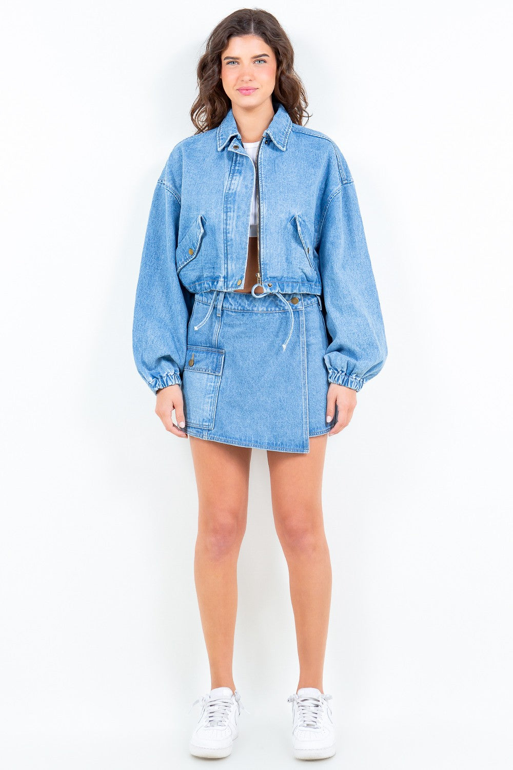 Woman wearing American Bazi drawstring waist crop denim jacket with zipper front and elastic cuffs, paired with a denim skirt.