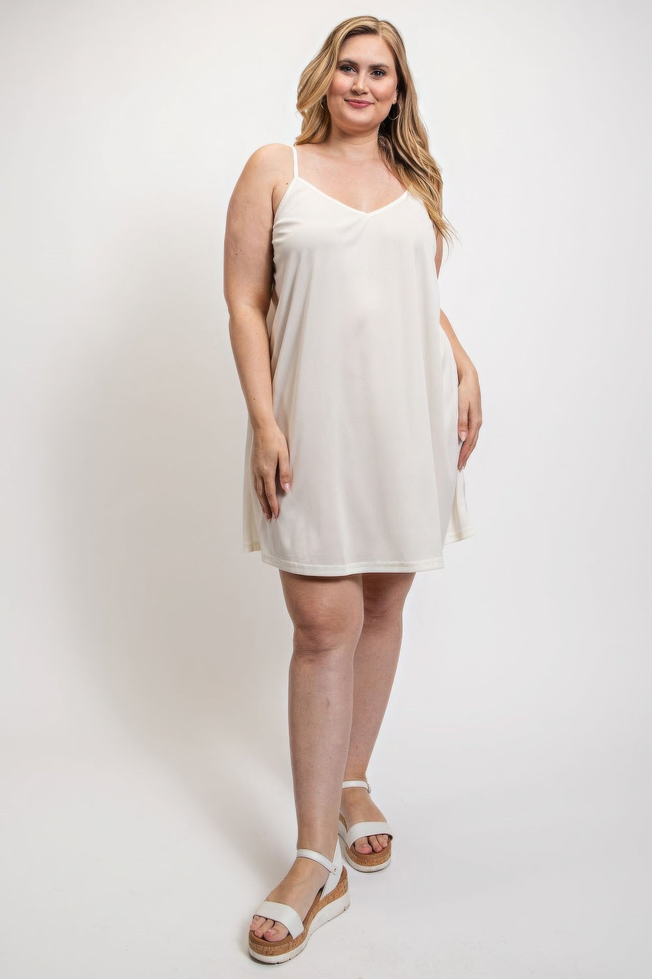 White V-neck slip dress with adjustable straps worn by woman, showcasing elegant and comfortable 100% polyester design.