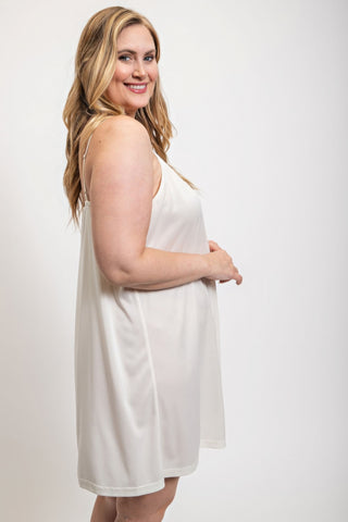 Woman wearing white V-neck slip dress with adjustable straps.