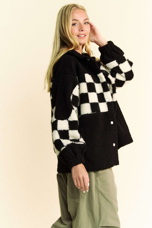 Black checkered faux fur jacket with snap-down buttons and pockets, made of 100% polyester, worn by a person standing sideways.