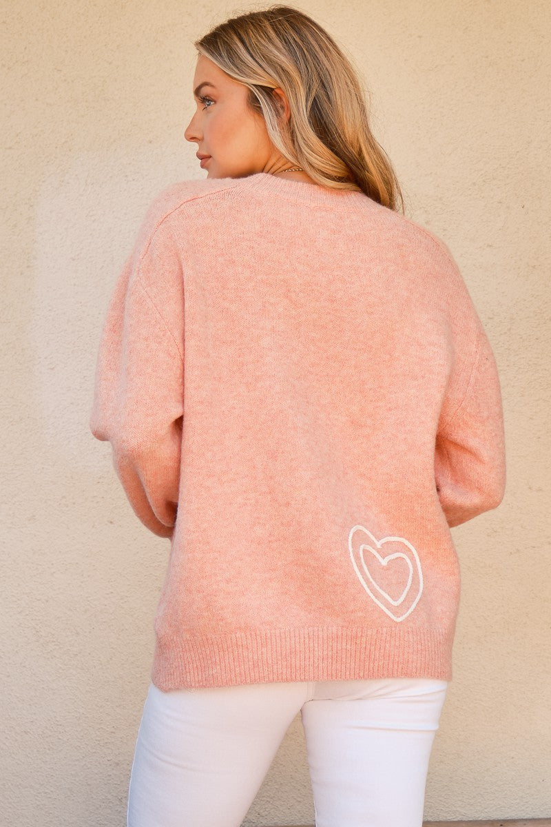 Woman wearing WIFEY & Heart round neck sweater in pink, featuring a white heart design on the back, paired with white pants.