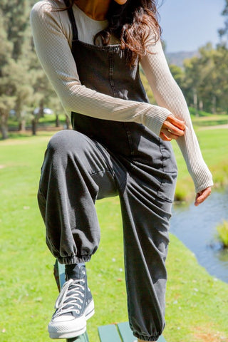 Woman wearing black drawstring waist spaghetti strap overalls with pockets, standing outdoors.