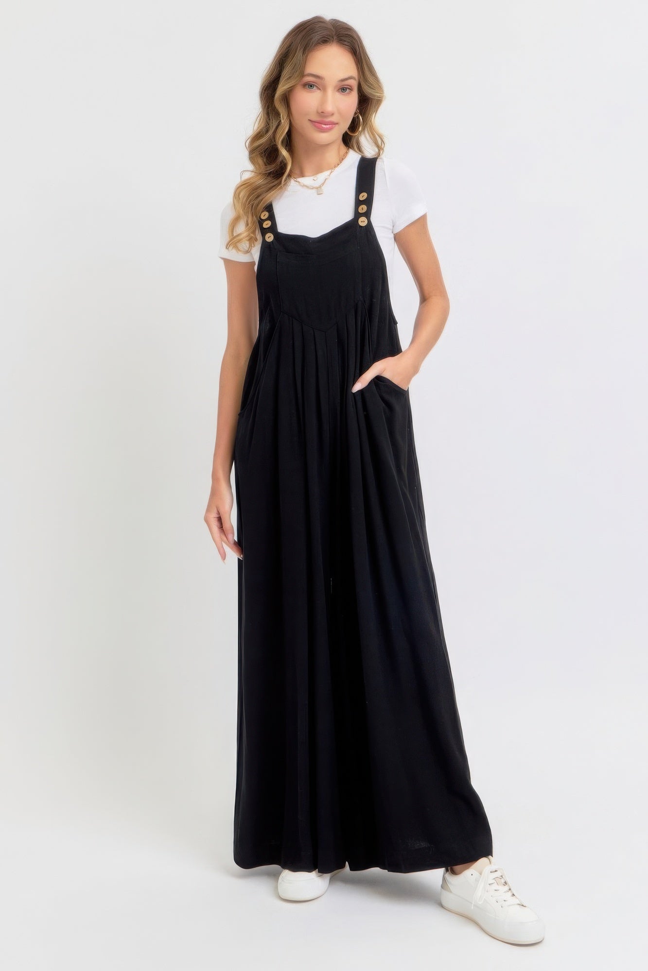 Woman wearing adjustable strap overall wide leg jumpsuit in black with a white top, showcasing a chic and relaxed style.