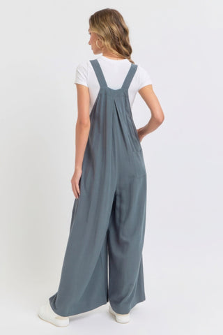 Woman wearing a chic adjustable strap overall wide leg jumpsuit in a solid color, showcasing a modern, relaxed silhouette from the back.