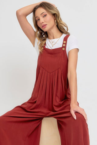 Woman wearing a chic red adjustable strap overall wide-leg jumpsuit with button details, showcasing a modern and relaxed vibe.