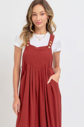 Woman wearing adjustable strap overall wide leg jumpsuit in rust color with a white top, showcasing a modern slouchy silhouette.